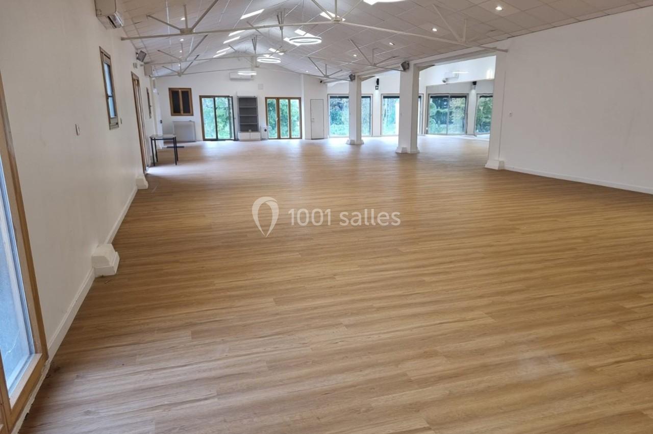 Salle spacieuse avec parquet en bois clair, grandes fenêtres et plafond incliné avec éclairage suspendu.