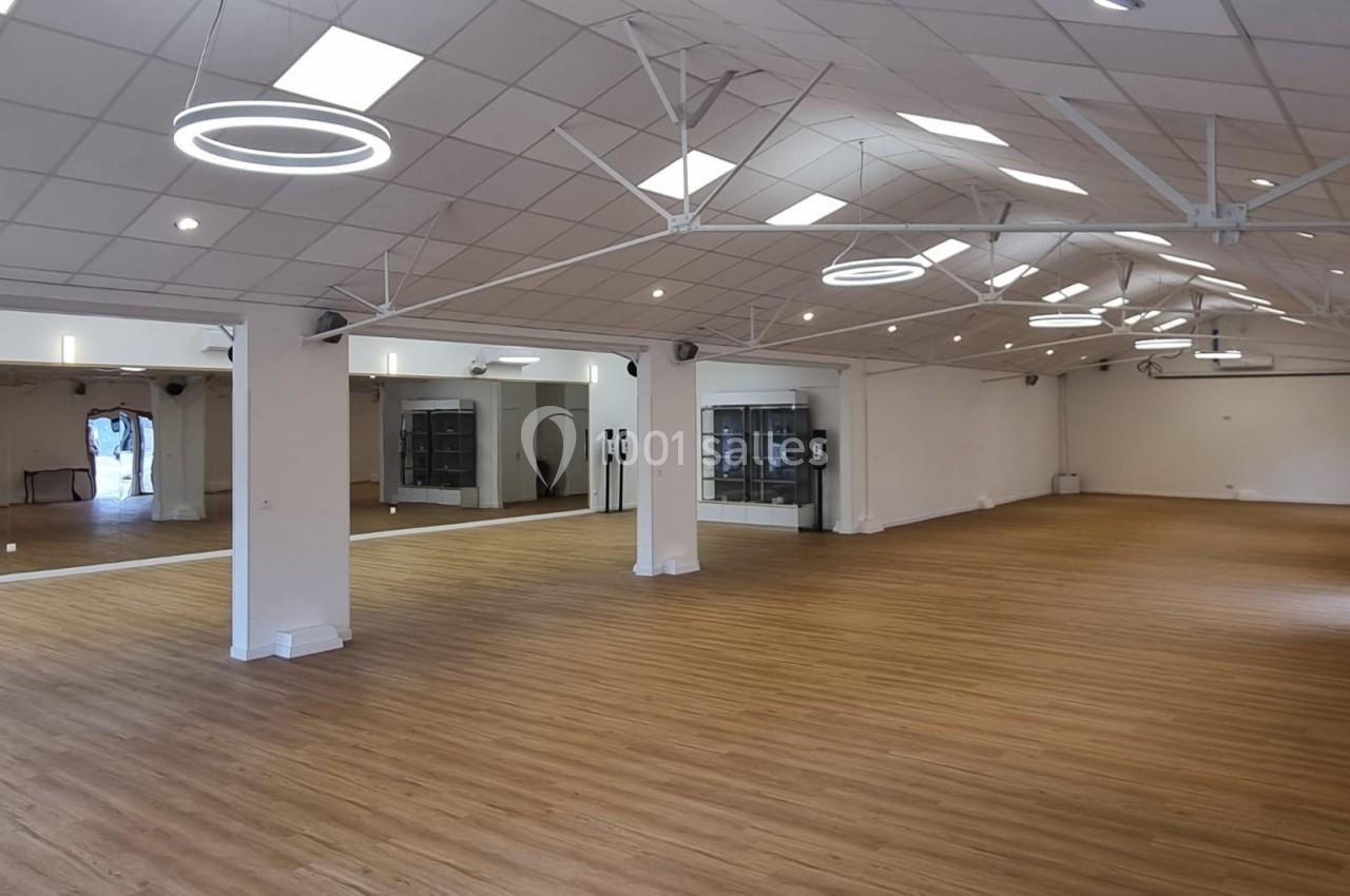 Salle spacieuse avec parquet en bois clair, murs blancs, miroirs et éclairage moderne suspendu.