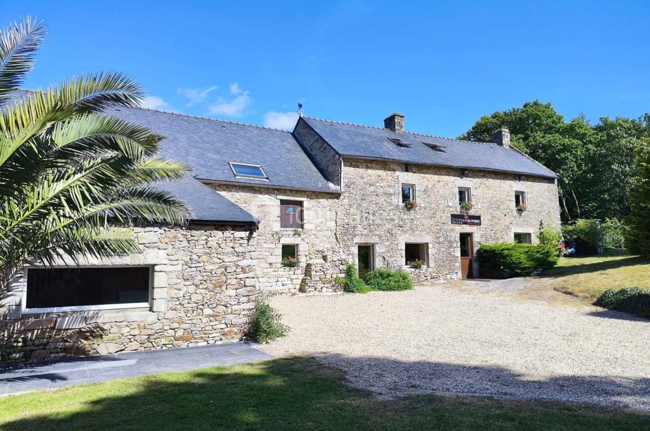 Façade d'une maison en pierre avec toit en ardoise, entourée d'un jardin et d'une allée gravillonnée.