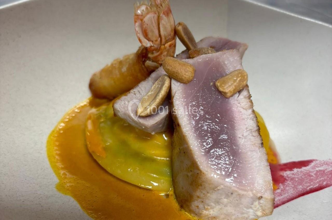 Tranche de thon mi-cuit accompagnée de sauce orange, crevette, gnocchi et amandes grillées dans une assiette blanche.