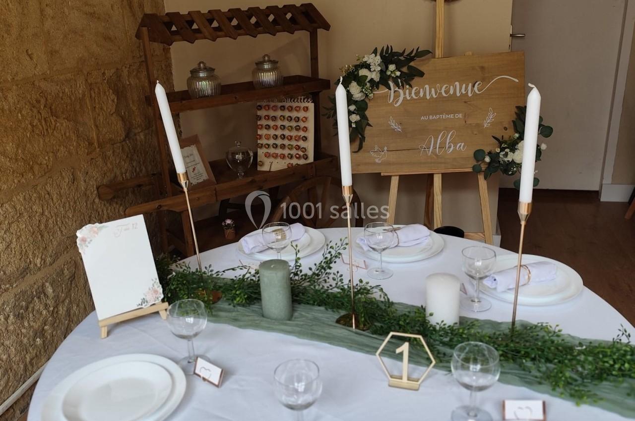 Table décorée pour un événement avec vaisselle blanche, bougies, verdure et panneau de bienvenue en arrière-plan.