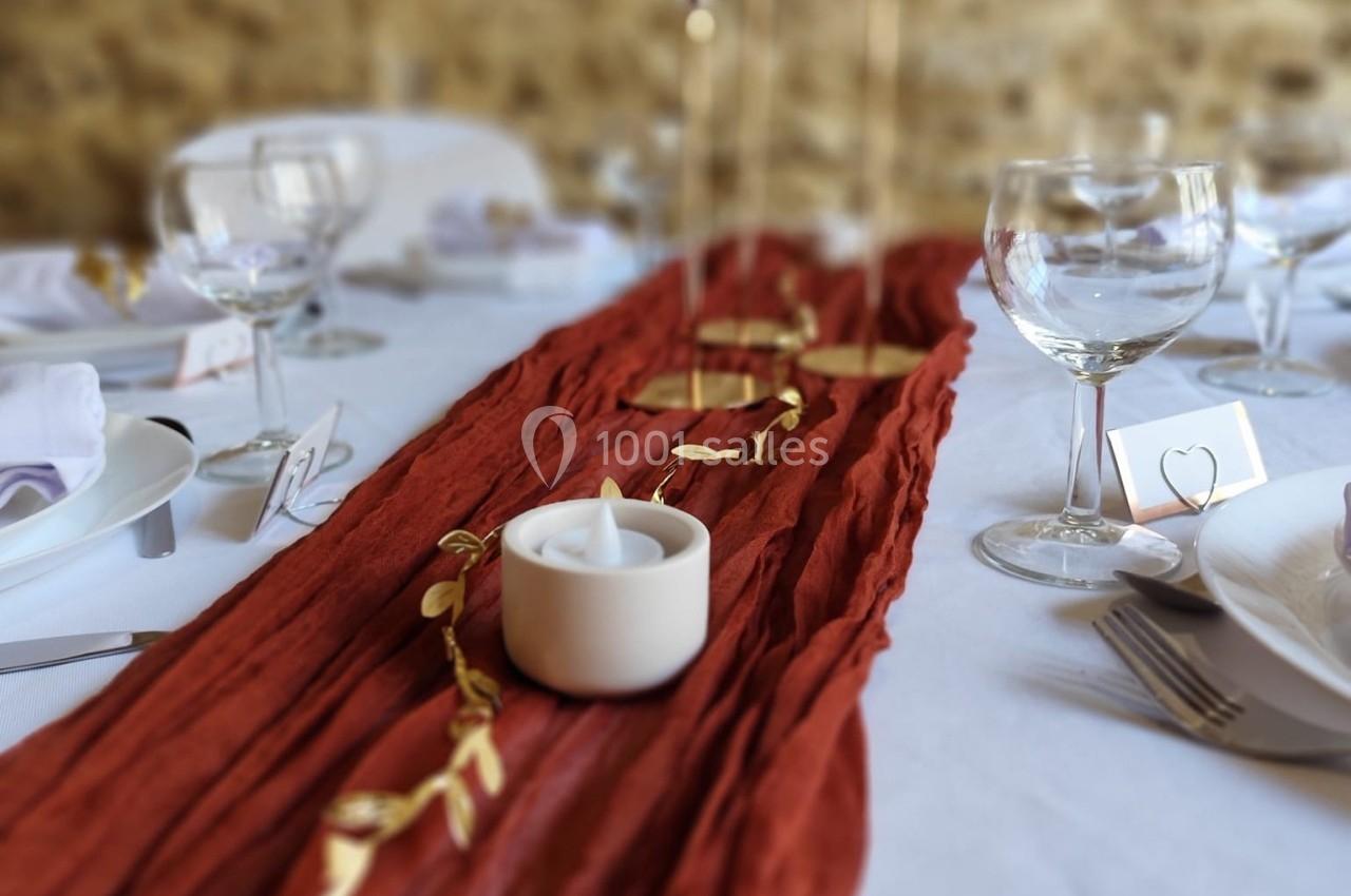 Chemin de table rouge texturé avec bougie blanche, décor doré et vaisselle disposée sur une nappe blanche.
