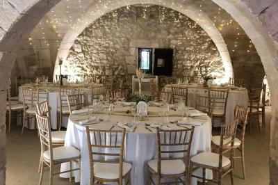 Salle de réception décorée avec des tables rondes dressées, nappes blanches et chaises ornées de nœuds beige.