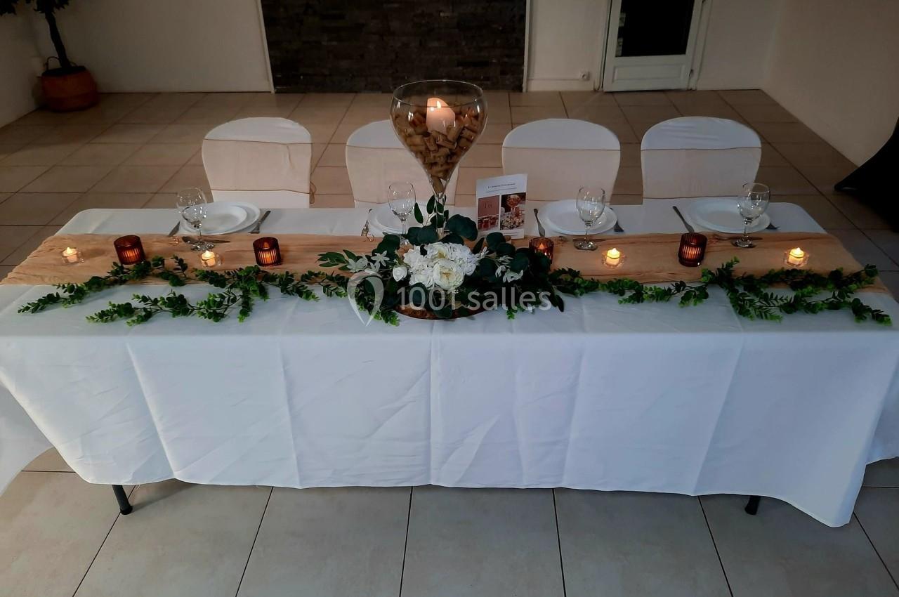 Table décorée avec une nappe blanche, centre de table floral, bougies et chemin de table beige dans une salle sobre.