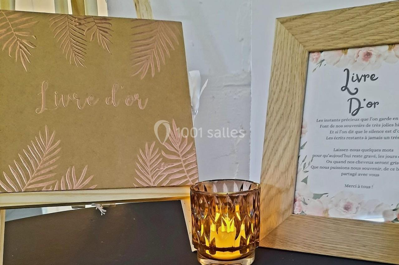 Livre d'or avec couverture dorée et cadre en bois contenant un texte, accompagné d'une bougie allumée.