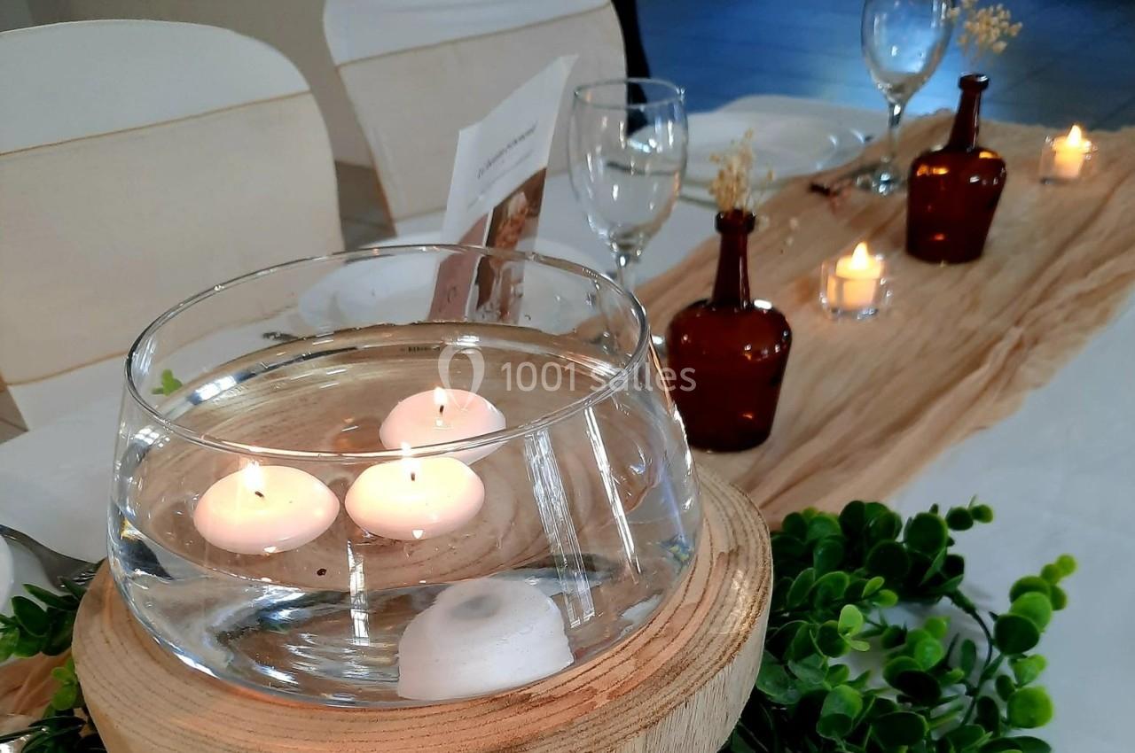 Bougies flottantes dans un vase en verre sur une table décorée avec des bouteilles marron et un chemin de table beige.
