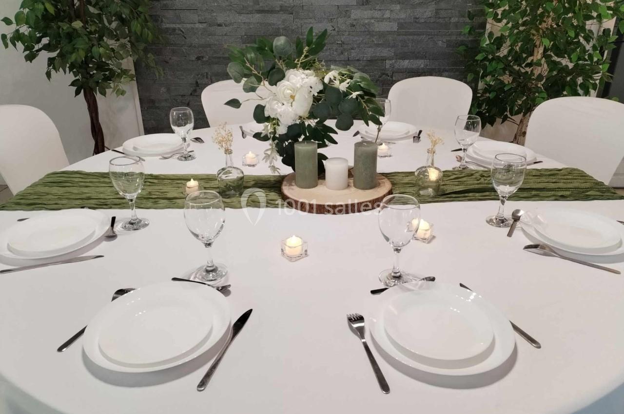 Table ronde élégamment dressée avec nappes blanches, chemin de table vert, bougies et centre de table floral.