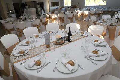 Salle de réception décorée avec des tables rondes dressées, nappes blanches et chaises ornées de nœuds beige.