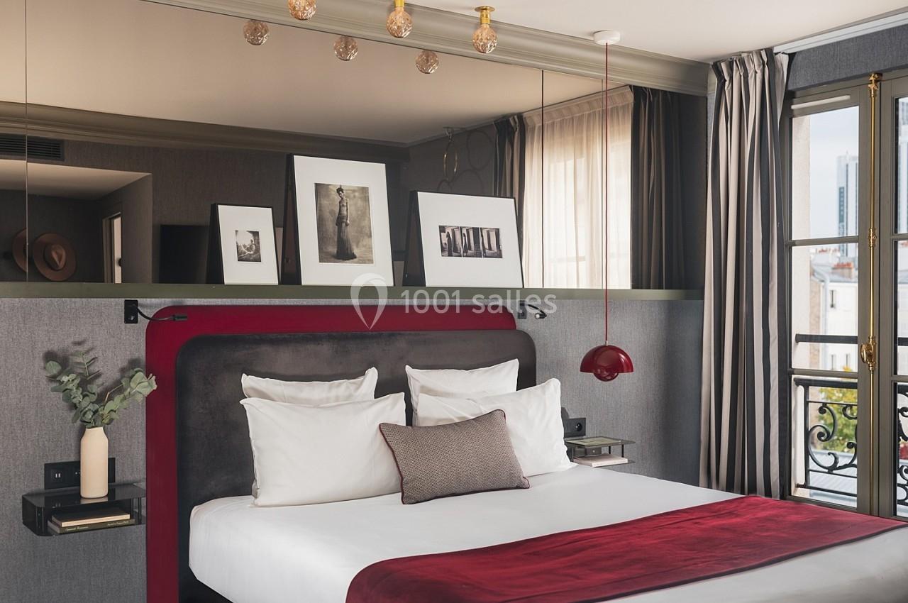Chambre élégante avec lit double, tête de lit rouge, décorations murales et fenêtre laissant entrer la lumière naturelle.