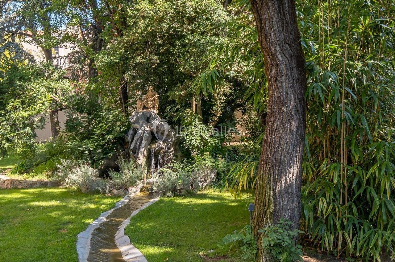 Un petit canal sinueux traverse une pelouse verdoyante, entourée d'arbres et de bambous dans un jardin paisible.