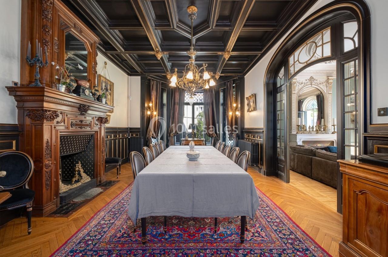 Salle à manger élégante avec table dressée, cheminée en bois sculpté, lustre et décorations classiques.