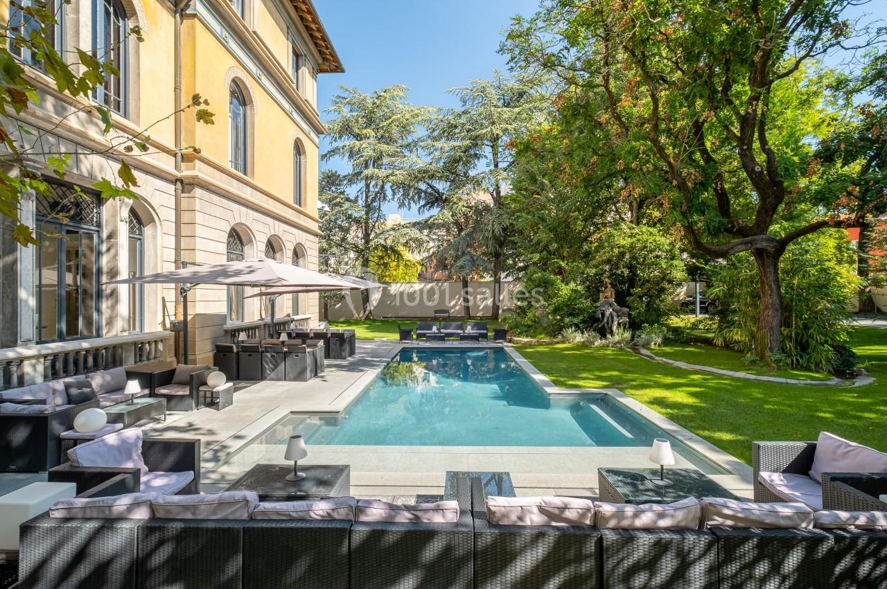 Piscine extérieure entourée de mobilier de jardin, située dans un espace verdoyant près d'une grande maison.