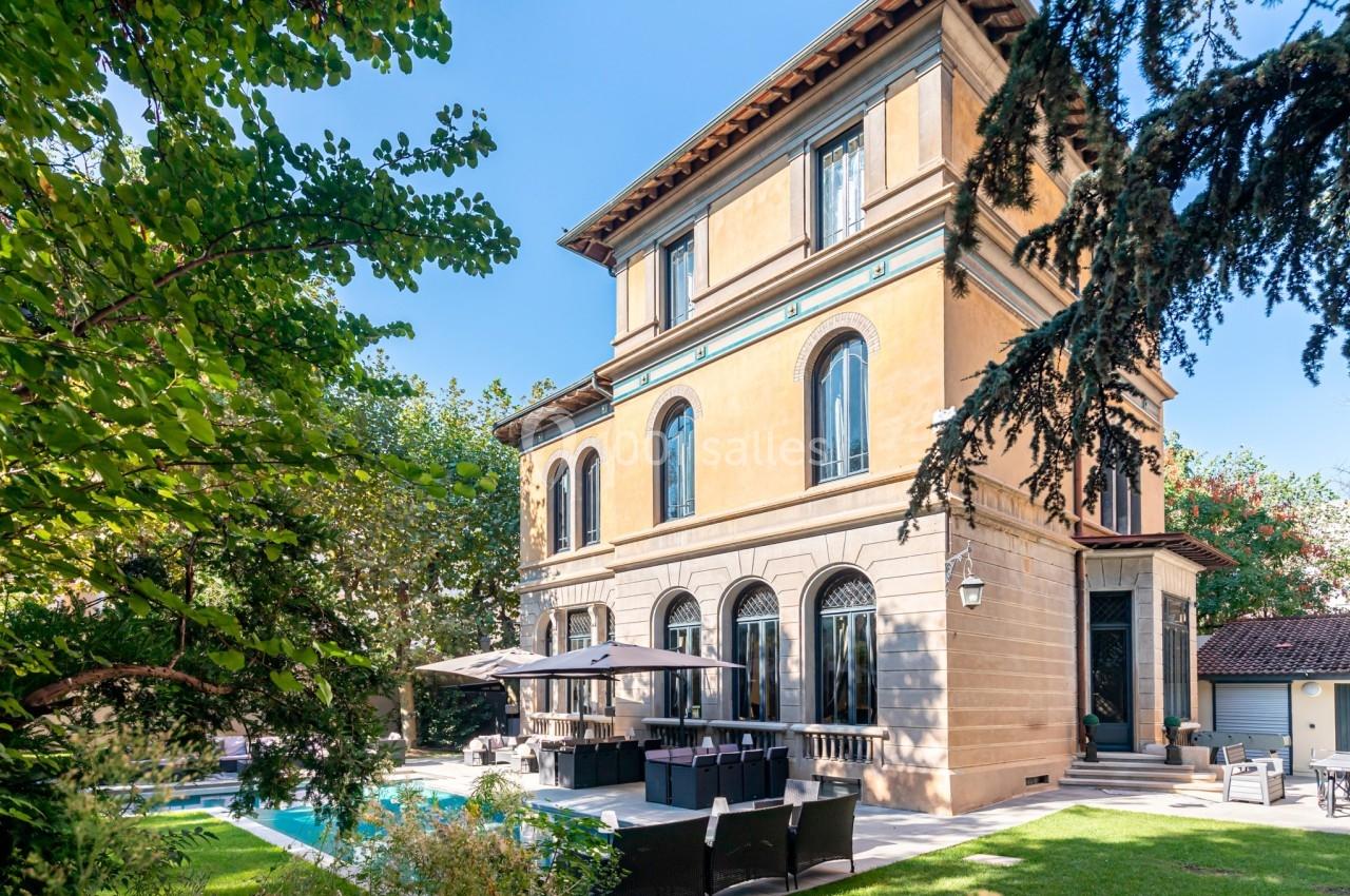 Grande maison de style classique avec jardin, piscine et terrasse aménagée, entourée de végétation.