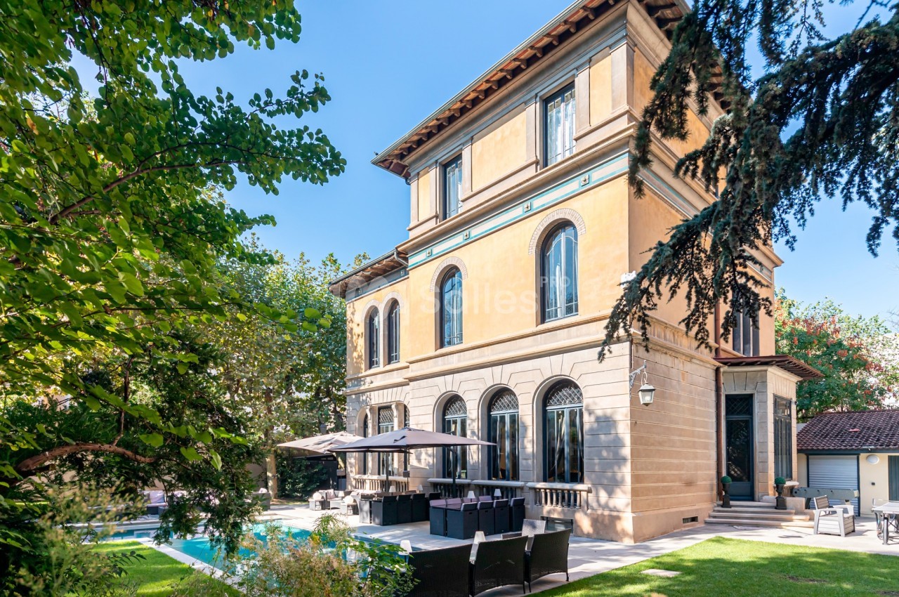 Grande maison de style classique avec jardin, piscine et terrasse aménagée, entourée de végétation.