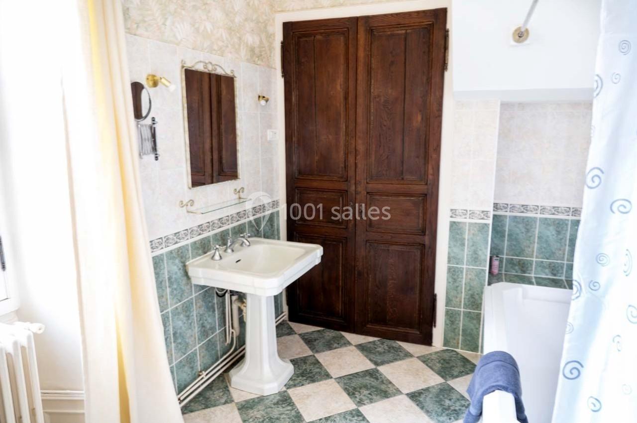 Salle de bain avec carrelage vert et blanc, lavabo sur pied, baignoire avec rideau et porte en bois sombre.