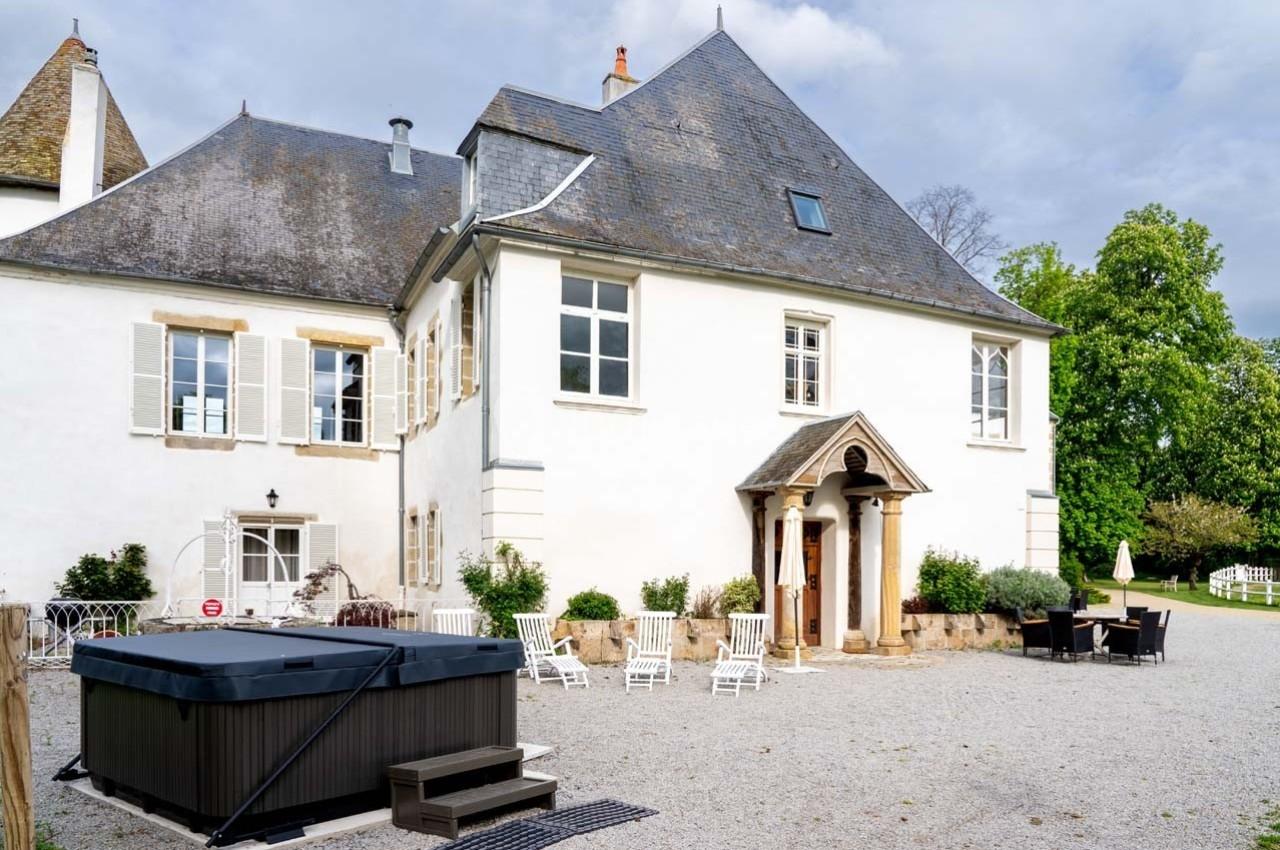 Façade d'une maison ancienne avec toit en ardoise, terrasse aménagée et jacuzzi dans une cour gravillonnée.