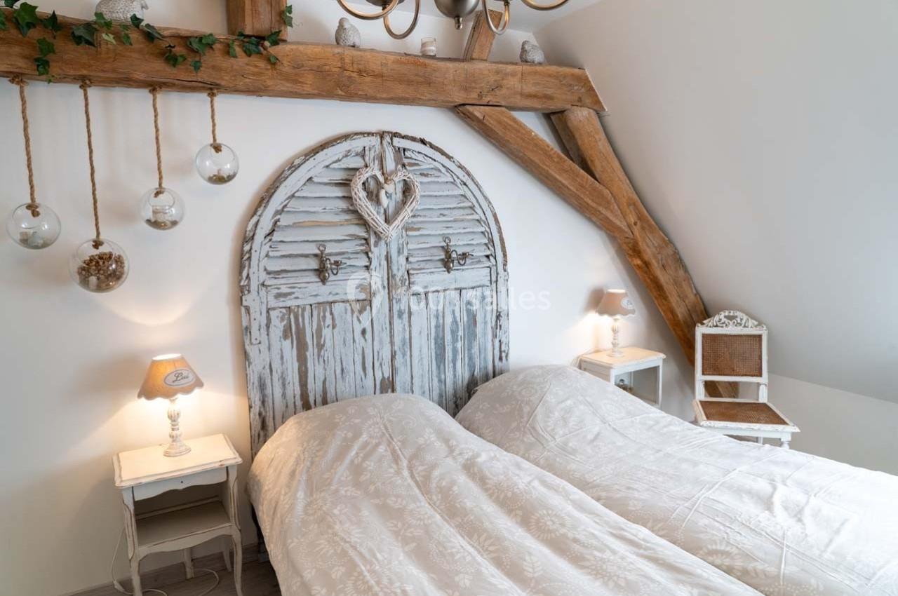 Deux lits simples avec une tête de lit en bois vieilli, entourés de lampes et décorations rustiques dans une chambre…