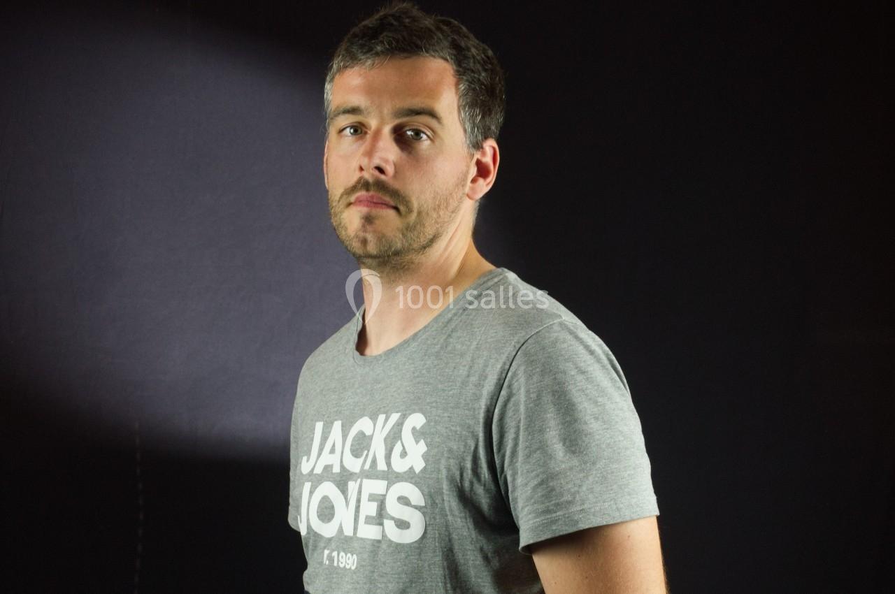 Homme portant un t-shirt gris avec un fond sombre et un éclairage latéral.