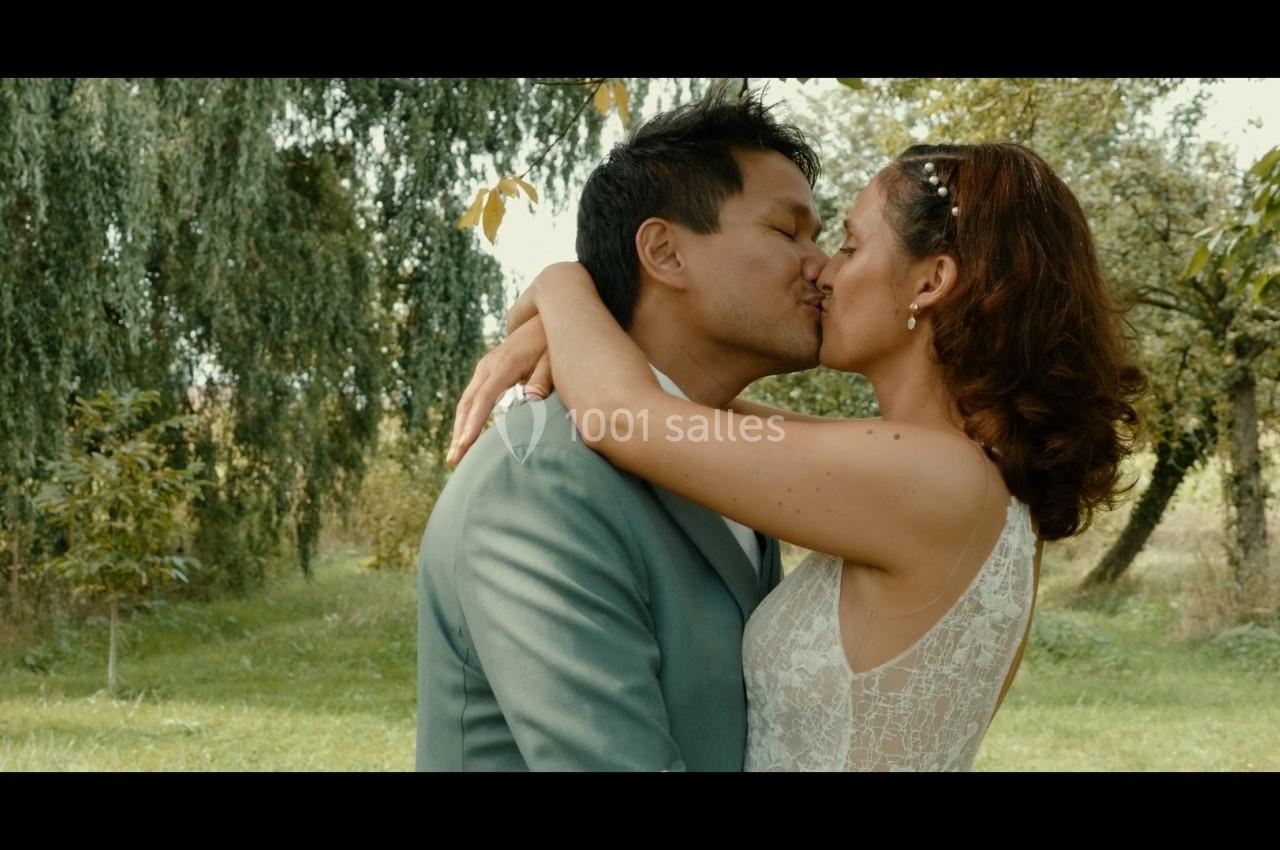 Un couple s'embrasse tendrement dans un jardin verdoyant, entouré d'arbres et de lumière naturelle.