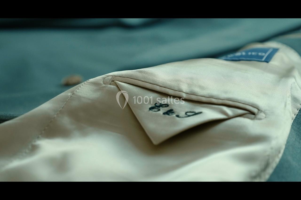 Poche intérieure d'une veste beige avec des initiales brodées en noir sur le rabat.