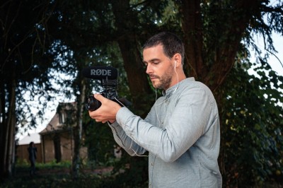 Un homme utilise une caméra équipée d'un microphone externe dans un environnement extérieur boisé.