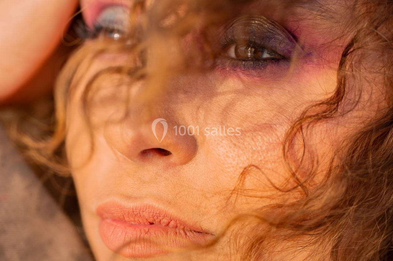 Femme au regard pensif, cheveux bouclés encadrant son visage, éclairée par une lumière douce.