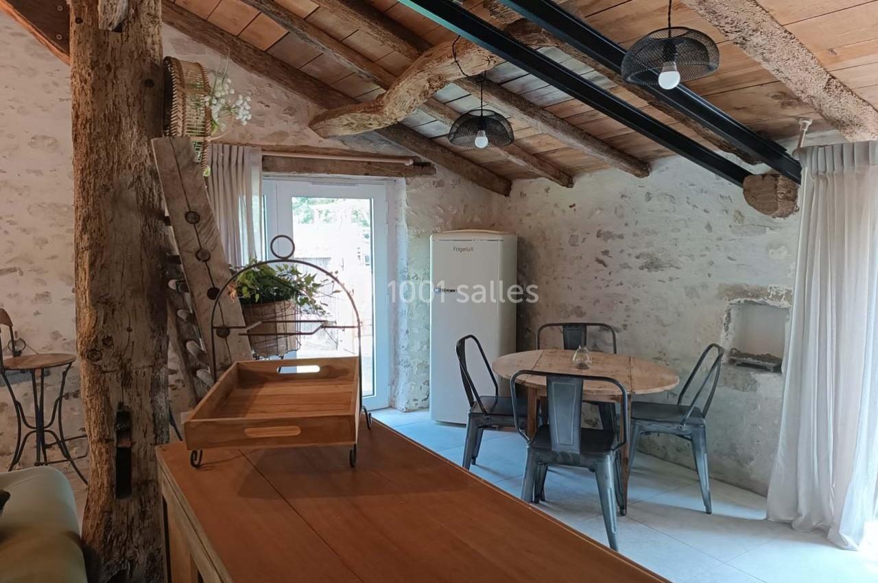 Cuisine rustique avec poutres apparentes, murs en pierre, table ronde en bois et chaises métalliques près d'une porte vitrée.