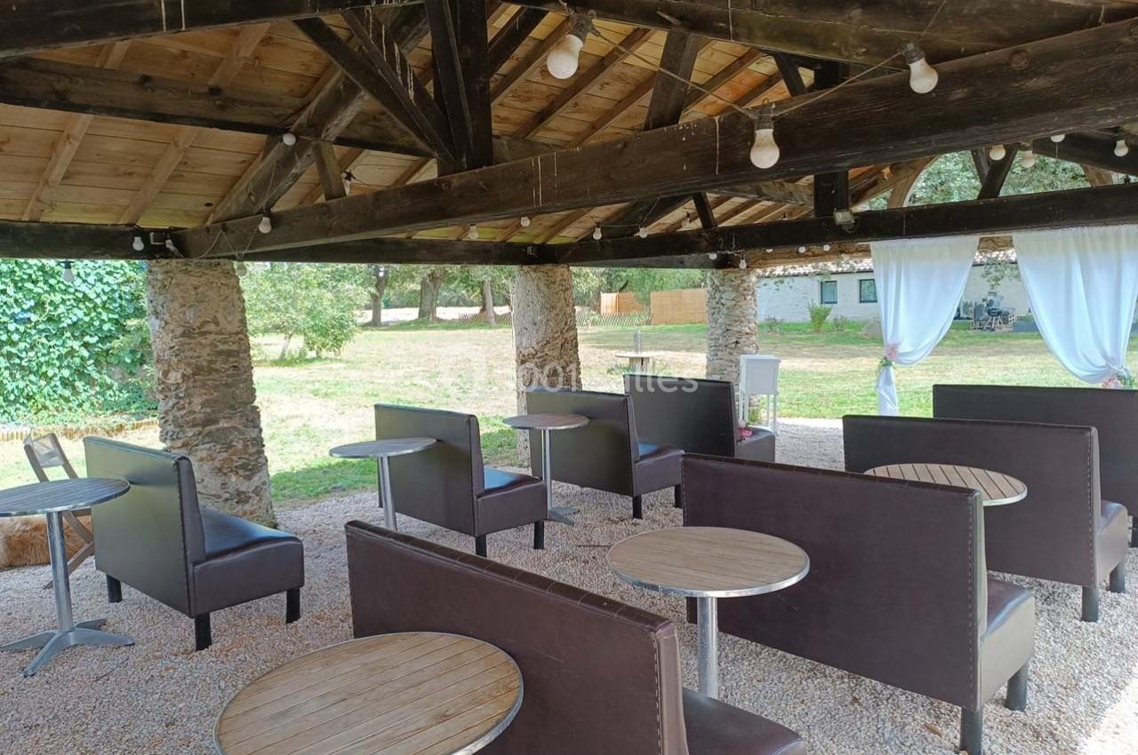 Banquettes et tables rondes disposées sous une pergola en bois, avec vue sur un jardin verdoyant en arrière-plan.