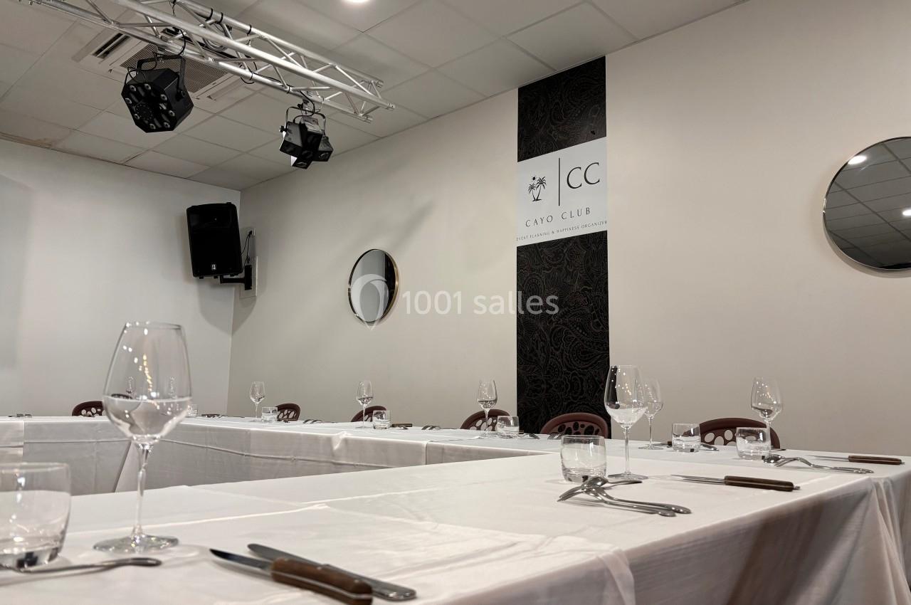 Salle de réception avec tables dressées, nappes blanches, verres et couverts, éclairage suspendu et miroirs muraux.