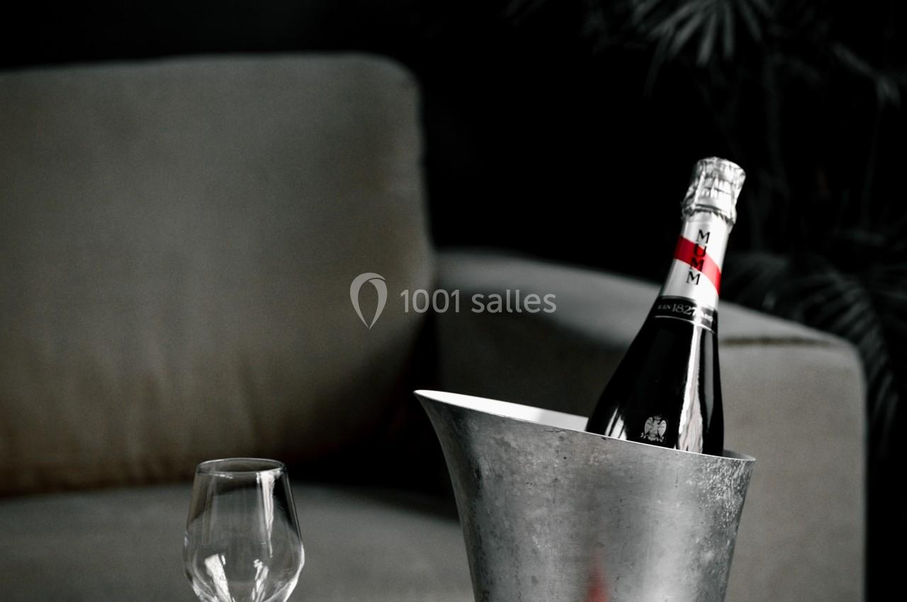 Bouteille de champagne dans un seau à glace, verre vide et fraises sur une table devant un canapé.