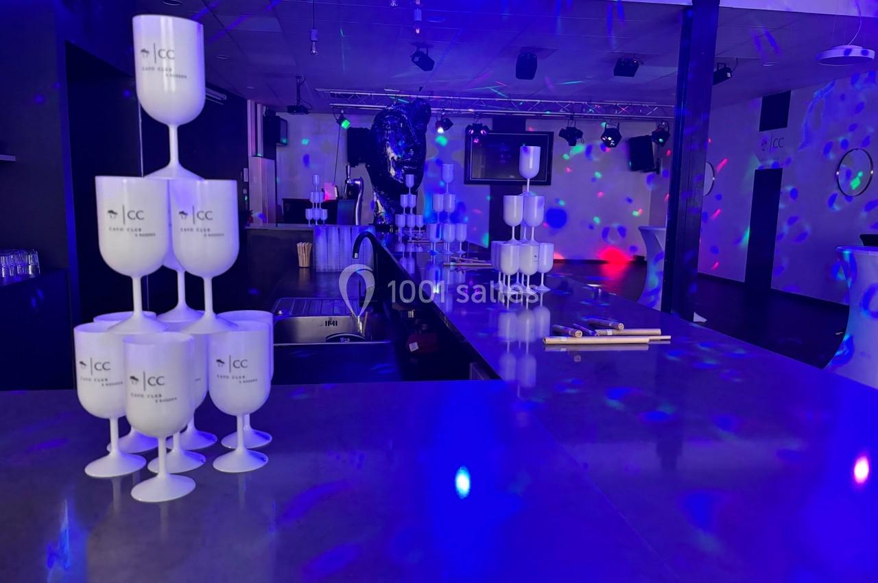 Salle de réception avec comptoir central, gobelets empilés et éclairage coloré créant une ambiance festive.