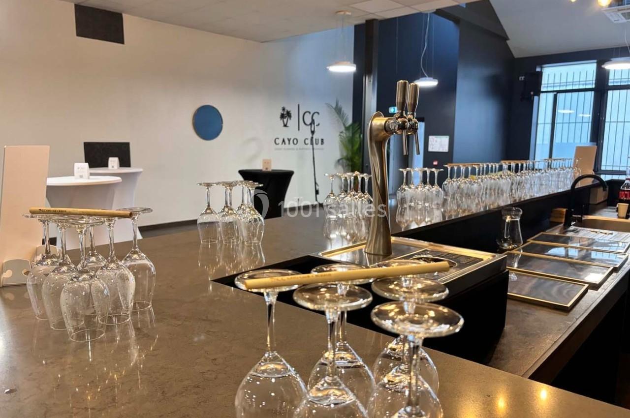 Salle de réception avec un bar équipé de verres à pied retournés et un robinet de bière, éclairée par une lumière naturelle.