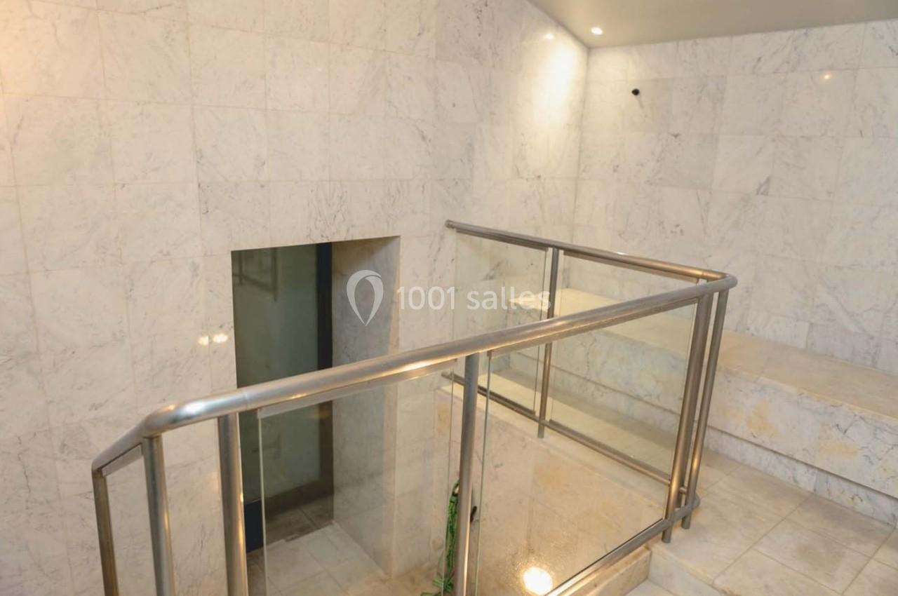 Escalier en marbre blanc avec rampe en métal et parois vitrées, dans un espace intérieur lumineux.