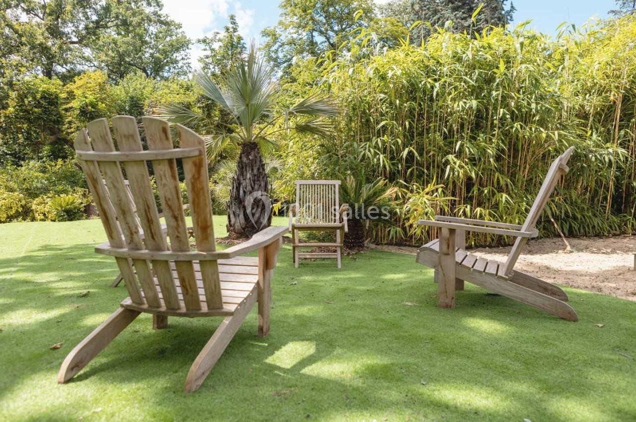Chaises en bois disposées sur une pelouse verdoyante, entourées de bambous et de végétation tropicale.