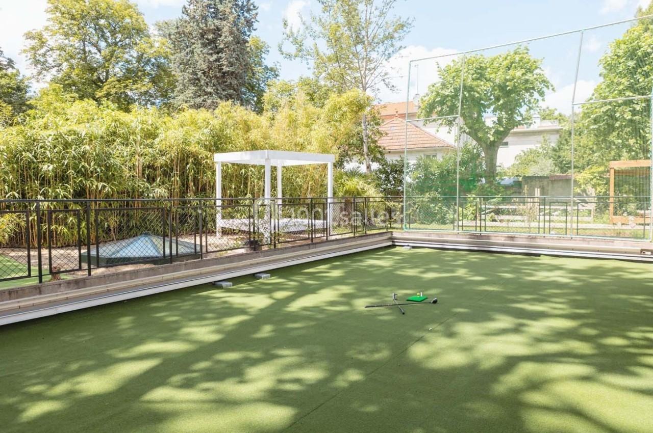 Terrain de sport extérieur en gazon synthétique entouré de végétation, avec un équipement posé au centre.