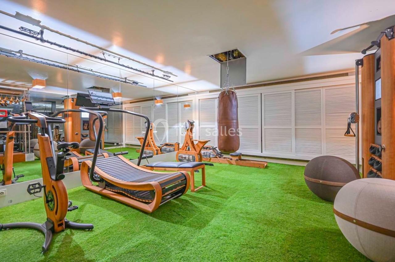 Salle de sport équipée avec machines en bois, sac de frappe, miroir mural et sol en gazon synthétique.