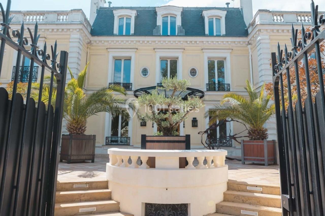 Façade d'un bâtiment élégant avec balcons, palmiers et portail noir ouvert au premier plan.