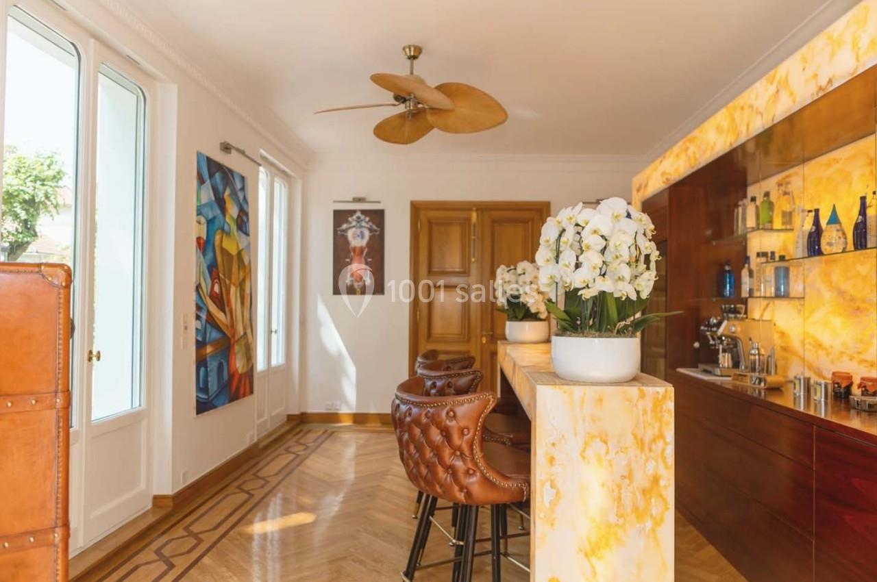 Intérieur lumineux avec un bar en onyx, tabourets en cuir, orchidées blanches et œuvres d'art sur les murs.