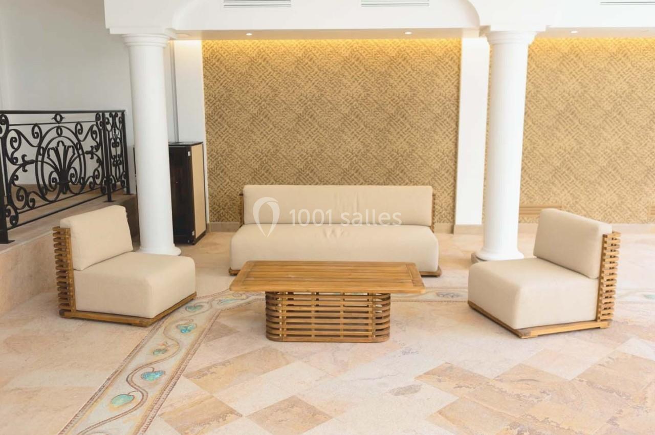 Mobilier de salon avec canapé, fauteuils et table basse en bois, disposés sur un sol en pierre beige.