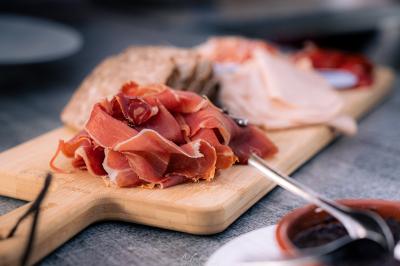 Miniature Location salle Sisteron (Alpes-de-Haute-Provence) - Restaurant le Segustero #4 Plateau en bois avec des tranches de jambon cru, pain et autres charcuteries, posé sur une table grise.