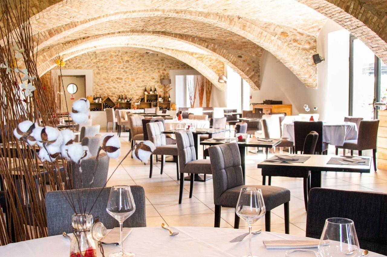 Salle de restaurant lumineuse avec des tables dressées, des chaises grises et un plafond voûté en pierre.