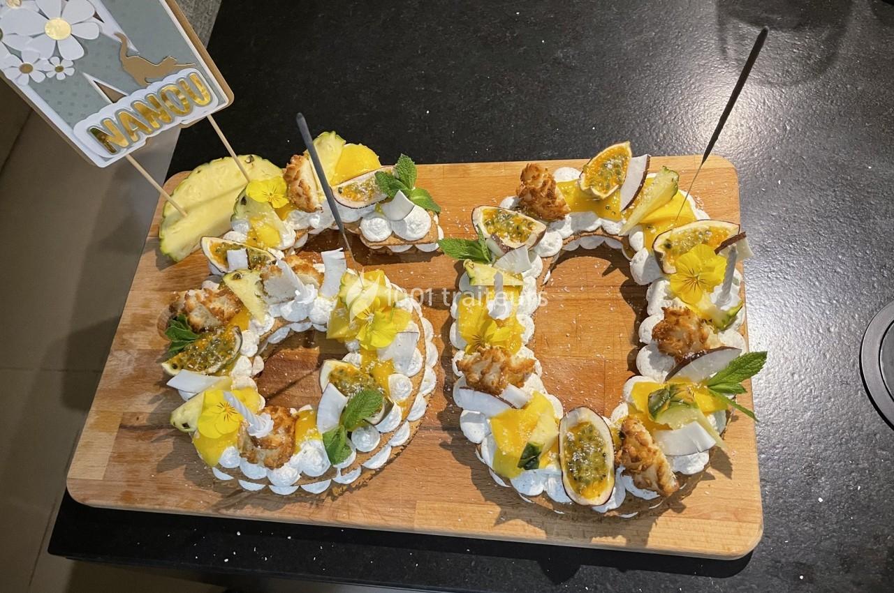 Couronnes de meringue garnies de fruits tropicaux, fleurs comestibles et décorations sur une planche en bois.