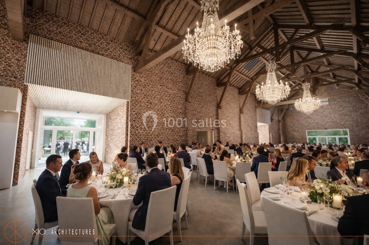 Salle de réception avec des invités assis à des tables décorées, éclairée par des lustres et entourée de murs en briques.