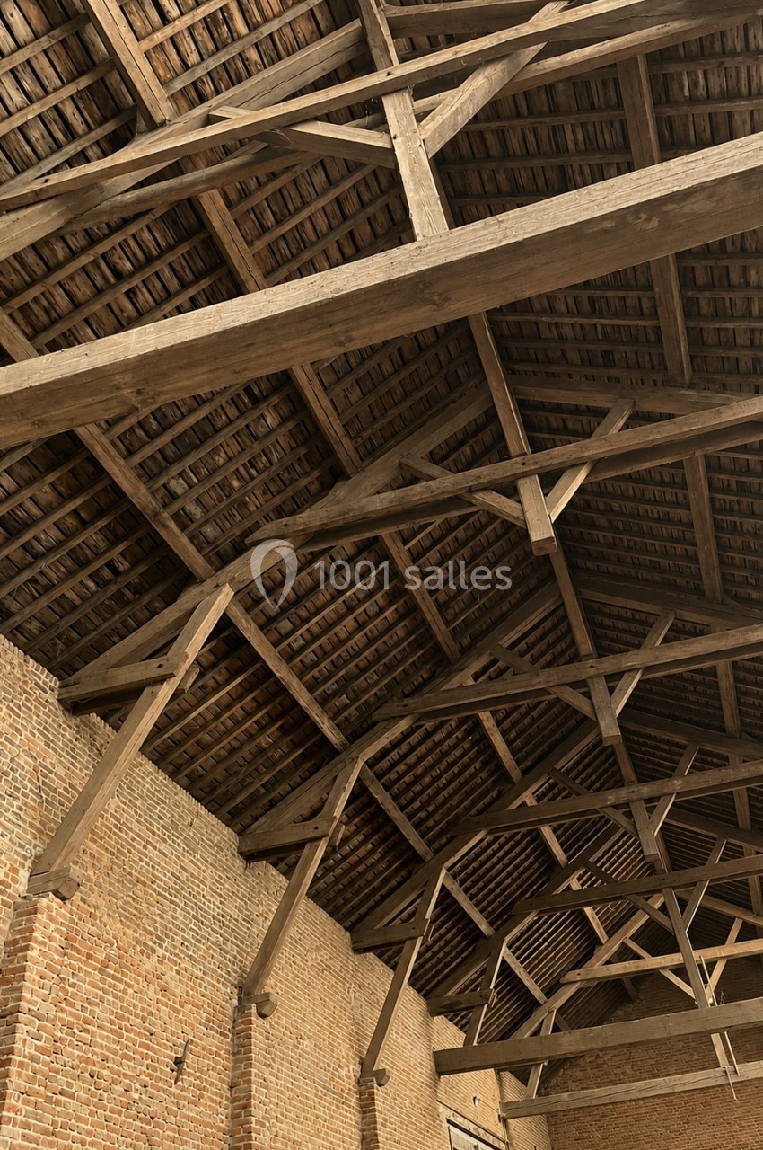 Charpente en bois apparente d'un bâtiment ancien avec murs en briques et toit en tuiles.