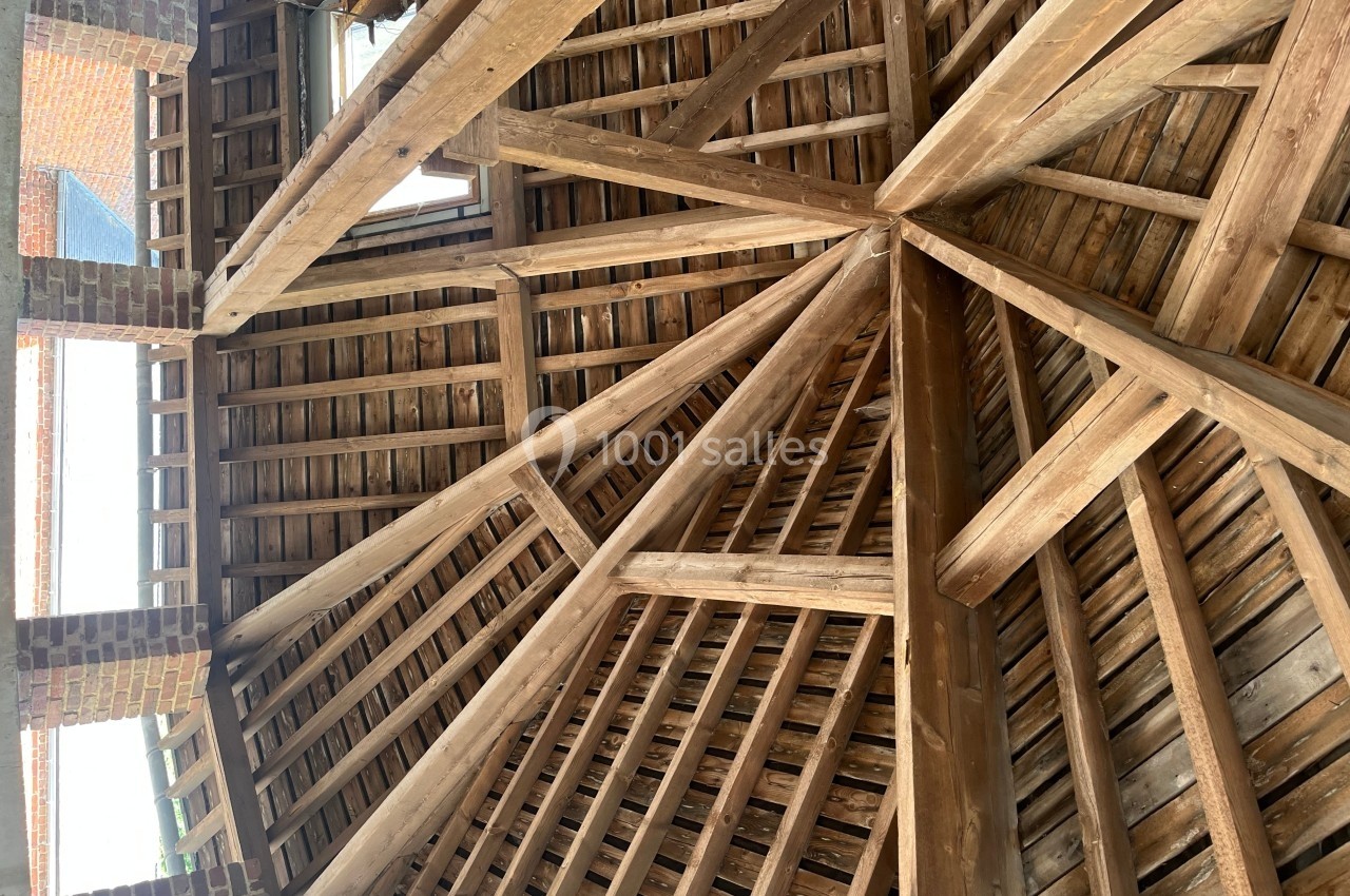 Charpente en bois apparente avec des poutres entrecroisées, vue depuis l'intérieur d'un bâtiment en briques.