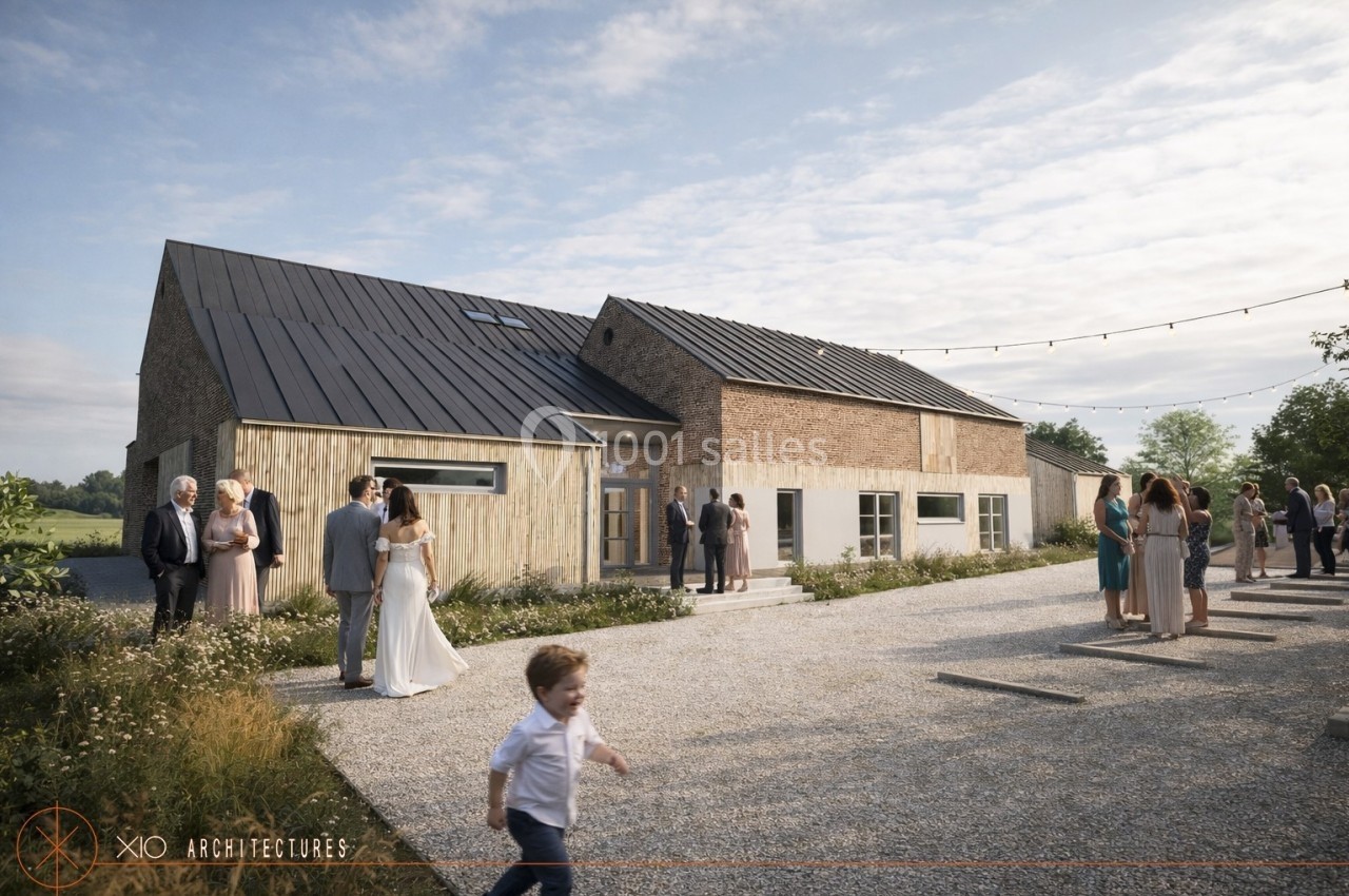 Un mariage en extérieur devant un bâtiment en briques et bois, avec invités discutant et un enfant courant au premier plan.