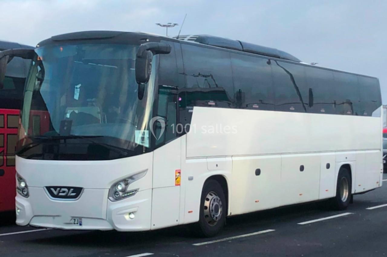 Autocar blanc stationné sur un parking, vu de côté, sous un ciel nuageux.