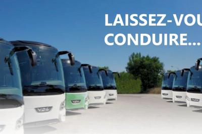 Autocar blanc stationné sur un parking, vu de côté, sous un ciel nuageux.