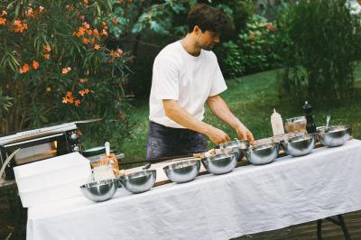 Miniature Traiteur Paris (Paris) - Pizzaiolo Tsogani #13 Un homme retire une pizza du four à l'aide d'une pelle, accompagné d'une femme souriante dans une cuisine moderne.