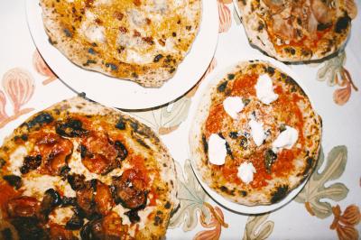 Miniature Traiteur Paris (Paris) - Pizzaiolo Tsogani #2 Un homme retire une pizza du four à l'aide d'une pelle, accompagné d'une femme souriante dans une cuisine moderne.